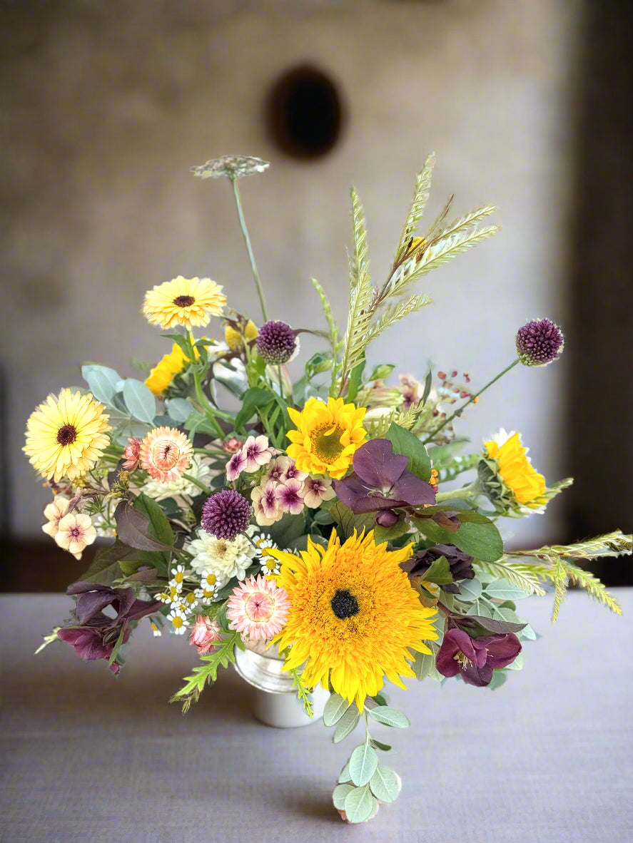 Bouquet of flowers with yellow sunflowers and greenery on a wooden surface.