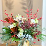 Decorative floral arrangement with red berries and green leaves in a gold vase on a wooden surface.