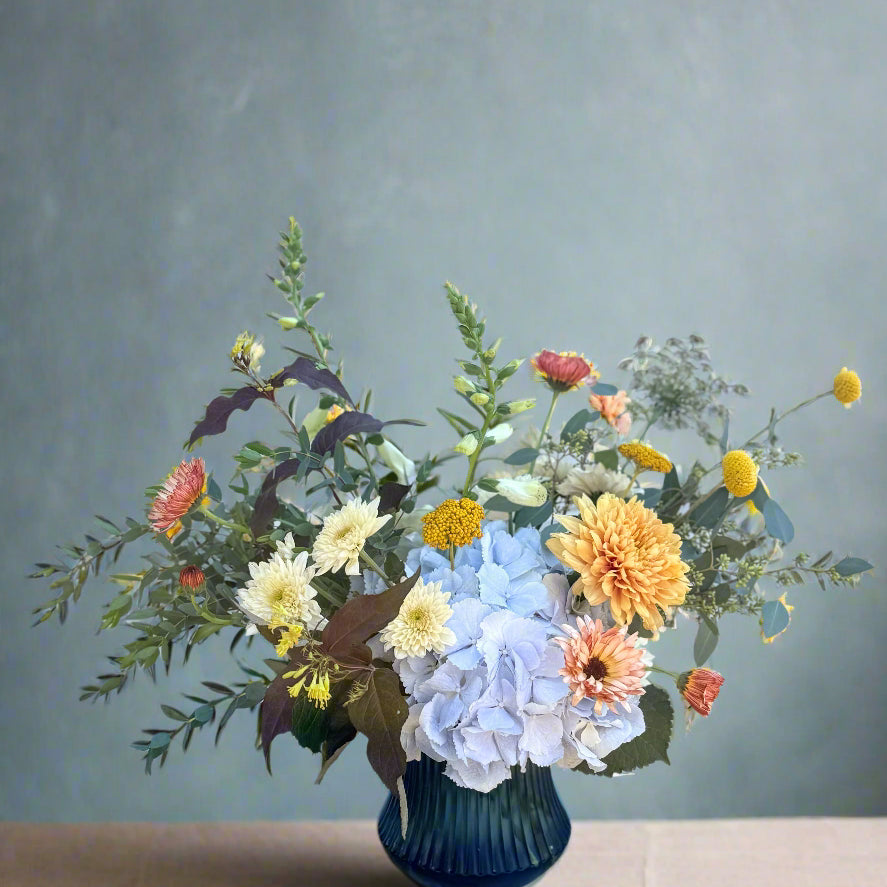 Bouquet of flowers in a blue vase on a wooden surface with a white brick wall background