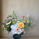 Floral arrangement in a blue vase on a wooden table with a light blue brick wall background