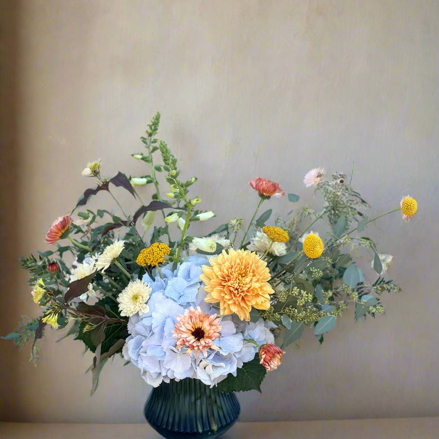Floral arrangement in a blue vase on a wooden table with a light blue brick wall background