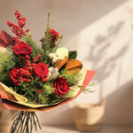 A bouquet of red roses, winter greens, magnolia, and berries.