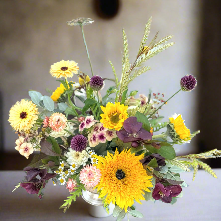 Bouquet of flowers with yellow sunflowers and greenery on a wooden surface.